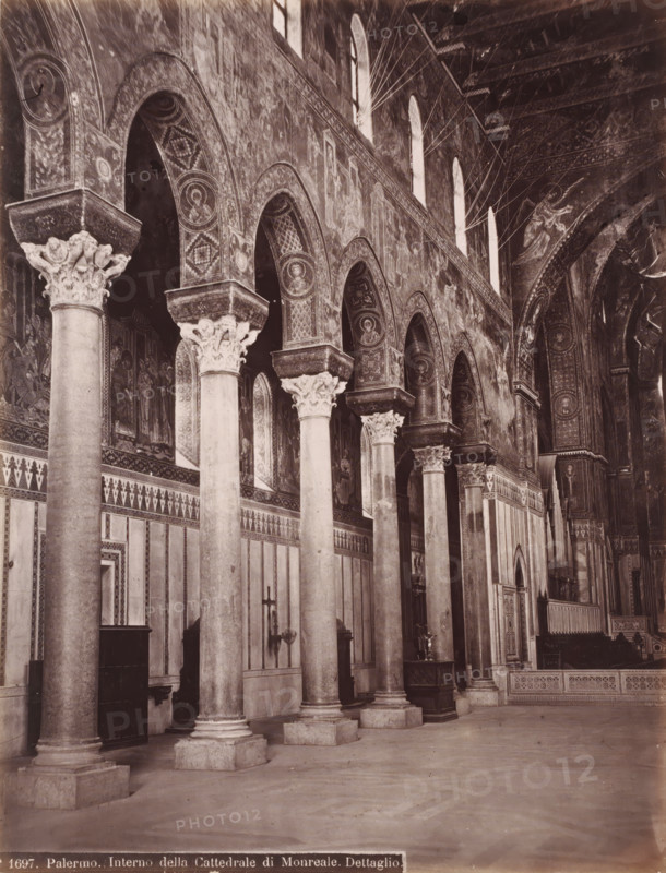 Interior of the Cathedral of Palermo, Italy, Interno della Cattedrale di Monreale. Dettaglio, Palermo, photograph, number: 'No 1697.', 1851 - 1900, photographer, Sicily, pasteboard, paper, albumen print, height 385 mm x width 309 mm, parts of church interior, Dom (Palermo), A wide interior view of a cathedral nave featuring a row of tall stone columns with ornate carved capitals supporting a series of rounded arches; the arches and upper walls are covered with detailed mosaics and painted medallions showing human figures and decorative patterns; narrow arched windows high on the wall allow light into the space; patterned friezes and rectangular panels decorate the lower walls; a few wooden furnishings and candle holders sit against the walls between the columns; the ceiling and upper arches display intricate ornamental designs and further figurative mosaics; the floor appears plain and open in the foreground.