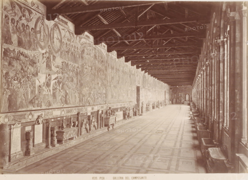 Galleria del Camposanto, Corridor in the Camposanto in Pisa, Italy, Pisa, photograph, number: '1020.', 1851 - 1900, photographer, Tuscany, pasteboard, paper, albumen print, height 309 mm x width 384 mm, wall-covering, gallery (spacious corridor), Piazza dei Miracoli, Camposanto (Piazza dei Miracoli), A long, vaulted interior space with a patterned floor and a high wooden beamed ceiling, one side lined with tall arches and columns and the opposite wall covered in large painted murals and decorative stone monuments mounted above a continuous bench, with sculpted reliefs and carved objects placed along the base and small windows or openings visible at the far end.