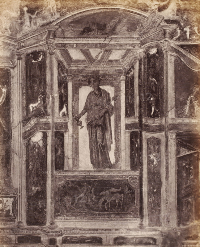 Photo reproduction of a fresco depicting a standing man in Pompeii, Italy, photograph, reproduction, number: '76.', inscription: 'Paroi Pompei', number: '11', Pompeii, after painting by anonymous, 1851 - 1900, photographer, pasteboard, paper, albumen print, height 403 mm x width 304 mm, picture, painting, wall-covering, A monochrome photograph of a painted wall panel showing a central tall niche containing a draped standing figure holding a long staff and a smaller object, flanked by architectural pilasters and decorative panels with classical motifs; above the niche is an ornate coffered arch with a small animal scene in the tympanum, and the surrounding panels contain faded figurative and ornamental paintings with worn textures, cracks, and areas of discoloration across the surface.