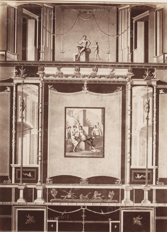 Photo reproduction of a fresco in Pompeii, Italy, photograph, reproduction, number: '84.', number: '11', Pompeii, after painting by anonymous, 1851 - 1900, photographer, pasteboard, paper, albumen print, height 403 mm x width 305 mm, picture, painting, wall-covering, A vertical section of an ornate wall with classical architectural details, featuring pilasters, columns, and decorative moldings. In the upper central panel, a framed scene shows a seated male figure holding a staff and a smaller standing figure nearby, with swags draped above. Below, a large rectangular panel contains a framed painting of several partially draped figures in a landscape setting. Flanking the central panels are tall niches and recessed doorways visible through vertical columns, with sculptural female figures mounted on tall staffs on either side. Ornamental friezes, medallions, and scrollwork run horizontally across the composition, while a lower register displays small sculptural figures engaged with anima...