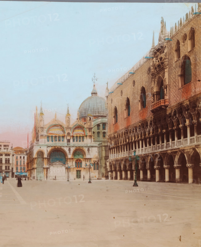 View of the Piazza San Marco towards the St. Mark's Basilica in Venice, Piazzetta dalle colonne, photograph, number: '52', Venice, 1851 - 1900, photographer, paper, albumen print, hand coloring, height 186 mm x width 242 mm, square, circus, church (exterior), parts of church exterior and annexes: campanile, St. Mark's Basilica, Doge's Palace, St. Mark's Square, A wide open paved square with a pale surface fills the foreground, leading to ornate historic buildings in the background; on the left a light-colored cathedral with domes and arched entrances shows decorative arches, columns, and sculpted details, while on the right a long facade of a brick building features rows of arched openings, colonnades, and carved ornamentation, with lamp posts standing along the square and a few small figures walking or standing near the buildings.
