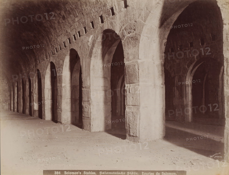Solomon's Stables, Solomonic Ställe, Ecuries de Salomon, Solomon's stables in Jerusalem, photograph, number: '384', Jerusalem, 1860 - 1900, photographer, paper, albumen print, height 211 mm x width 277 mm, ritual practices, Islam, Mohammedanism, A long covered stone corridor with a series of tall rounded arches supported by thick rectangular pillars receding into the distance, a vaulted ceiling with small rectangular openings near its upper edge, rough textured stone surfaces on the arches and walls, deep shadowed recesses visible through the arches, a sandy floor with scattered small debris, and light creating bright areas on some pillars and the floor.
