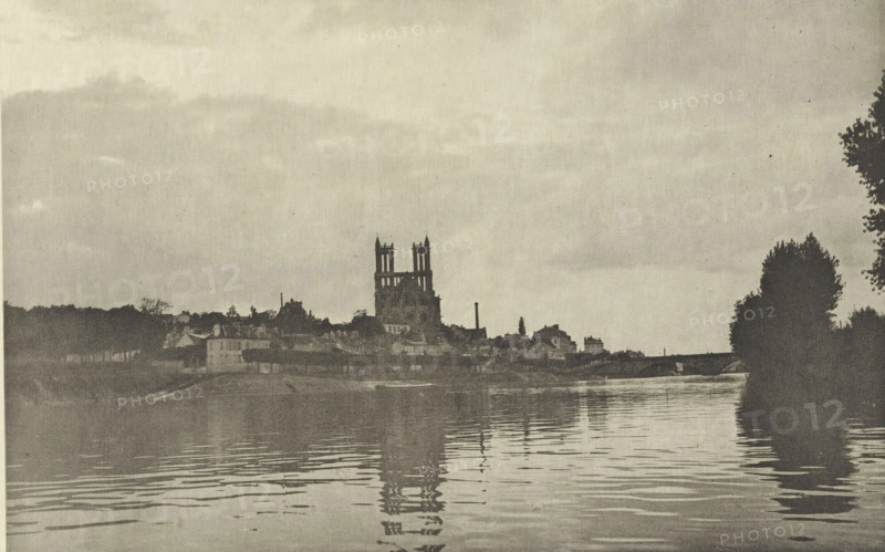 View of Mantes in the evening, Le Soir, à Mantes, photomechanical print, photographer: Achille Darnis, Limay, cliché maker: Fillon & Heuse, printer (person): Charles Wittmann, Paris, c. 1891 - in or before 1896, printer (person), paper, photoaquatint, height 129 mm x width 199 mm, city-view in general, 'veduta', river, dusk, evening twilight, Seine, Mantes-la-Jolie, A riverside scene in a muted monochrome palette shows a calm body of water in the foreground with gentle ripples reflecting dark vertical shapes. Across the water a low town silhouette stretches along the bank with clustered buildings and varied rooflines. A large structure with twin tower-like forms rises above the other buildings near the center, its vertical outlines mirrored faintly in the water. Trees and taller vegetation frame the right edge of the image as darker masses, and a broad sky occupies the upper portion with soft, diffuse cloud tones.