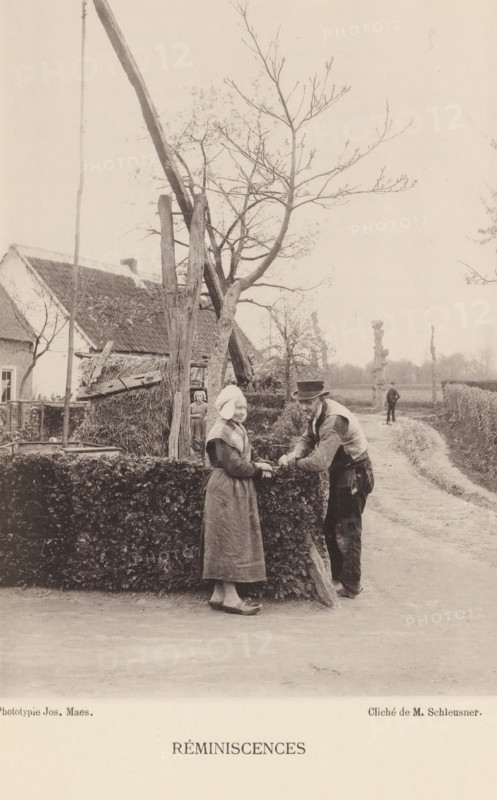 Man and woman at a farm, Réminiscences, page, photomechanical print, inscription: 'Section d'Anvers - Exposition de 1889', photographer: Henri Schleusner, cliché maker: Joseph Maes, printer (person): Joseph Maes, Antwerp, c. 1883 - in or before 1888, Henri Schleusner, Joseph Maes, photographer, cliché maker, printer (person), paper, collotype, photoprint, height 156 mm x width 115 mm, Print on unnumbered page., farmers, farm (building), A sepia-toned outdoor scene shows a dirt road curving past a trimmed hedge and a thatched rural house with a pitched roof; a leafless tree with thin branches rises behind a wooden framework and a tall pole near the house; a woman in a long dress and head covering stands at the hedge facing a man who leans on the hedge wearing a hat and work clothes, their hands near each other; in the background a child stands partially hidden by the hedge and another figure walks on the road farther away beneath a pale sky.