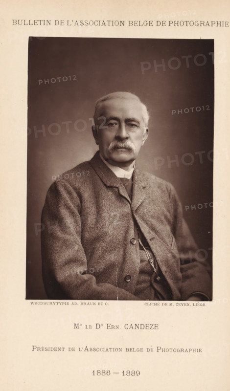 Mr. le Dr. Ern. Candeze. Président de l'Association Belge de Photographie (1886-1889), Portrait of Ernest Candèze, president of the Association belge de Photographie, page, photomechanical print, photographer: Léonard Hubert Zeyen, cliché maker: Adolphe Braun & Cie., printer (person): Adolphe Braun & Cie., Dornach, 1886 - 1889, Léonard Hubert Zeyen, Adolphe Braun & Cie., photographer, cliché maker, printer (person), Mulhouse, paper, Woodburytype, height 144 mm x width 102 mm, Print on unnumbered page., Person, Ernest Candèze, historical persons, adult man, chairman, A sepia-toned portrait of an older man seated and facing forward, shown from the waist up against a plain dark background, with short light hair, a full mustache, and rimless glasses; he wears a textured jacket over a buttoned waistcoat and a high-collared shirt, and his hands rest in his lap with a faint crease or line visible on the lower part of the photograph; the portrait is centered within a wider lighter-toned page t...