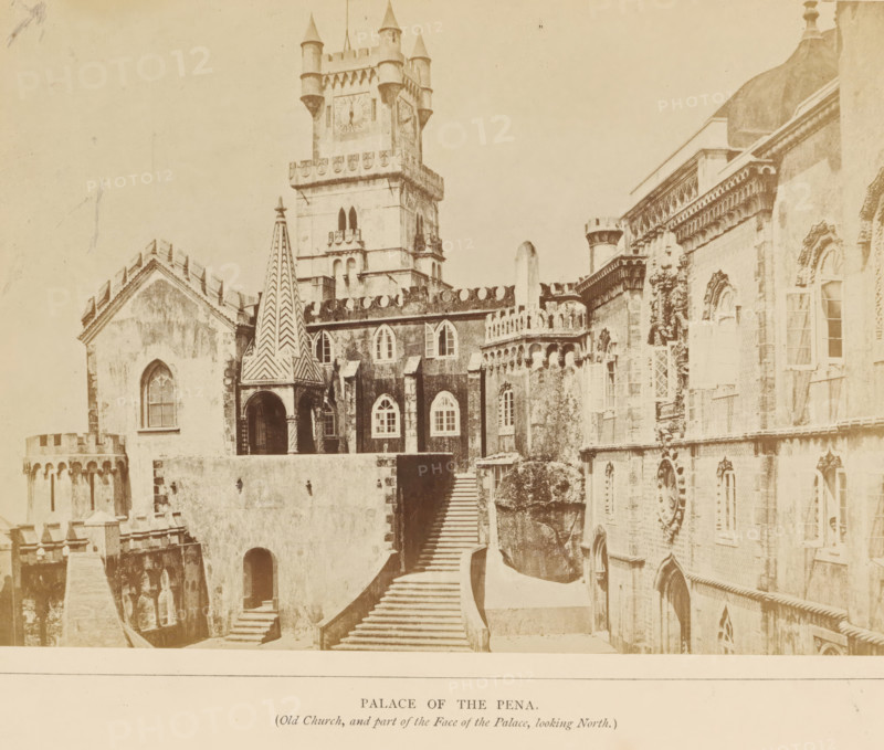 Palace of the Pena (Old church, and part of the Face of the Palace, looking north), View of the Palácio da Pena in Sintra, photograph, page, Sintra, c. 1865 - in or before 1870, photographer, paper, albumen print, height 142 mm x width 200 mm, Photo on second unnumbered page after page 24., palace, Palácio da Pena, A sepia photograph of a palace facade showing ornate stone architecture with battlements, arched windows, and decorative stonework; a tall square clock tower with turrets and crenellations rises above the buildings; a narrow conical turret with a patterned surface stands near an arched entrance; a wide stone stairway leads up between walls to the higher level of the complex; rounded and pointed window openings with shutters and tracery appear on several facades; carved ornamental details and cornices decorate the exterior walls; portions of domed and cylindrical rooftop elements are visible against a pale sky.