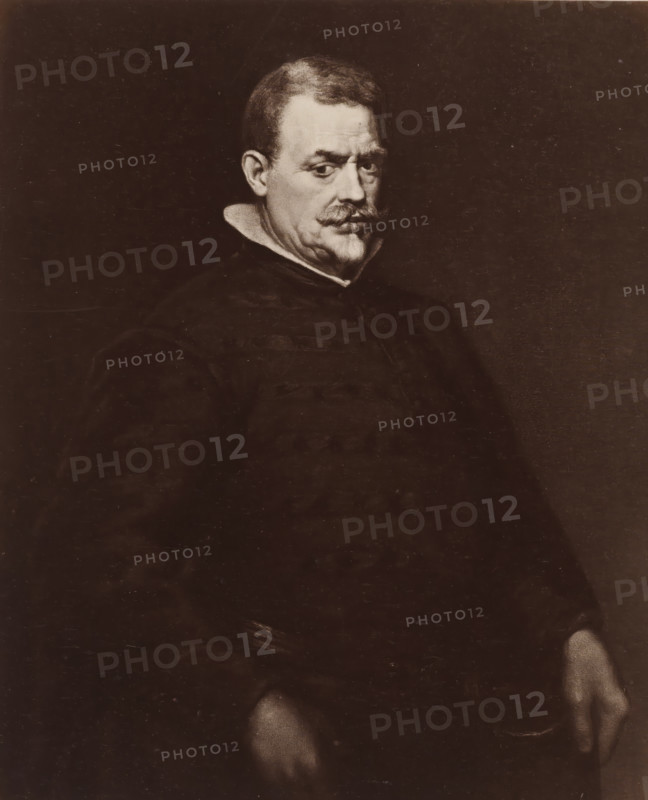 Photo reproduction of a painted portrait of Don Juan Mateos by Diego Velázquez, D. Velasquez: Männliches Bildniss, photograph, reproduction, page, after painting by Diego Rodriguez de Silva y Velázquez, publisher: Photographische Gesellschaft Berlin, Berlin, c. 1870 - in or before 1875, photographer, paper, albumen print, height 211 mm x width 175 mm, Photo on unnumbered page., Person, Juan Mateos, historical persons, A sepia-toned portrait of a man seated against a dark background, showing his head and upper body turned slightly to one side, with short hair and a prominent mustache, a high white collar visible at his neck, dark clothing with broad shoulders, and hands resting at his sides, one hand partially visible at the lower edge of the image.