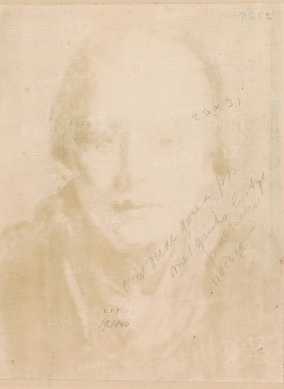 Portrait of an unknown young woman with a bonnet, print, printmaker: Frans Deutmann (signed by artist), 1877 - 1915, paper, monotype, printed in brown, height 326 mm x width 259 mm, anonymous historical person portrayed alone - BB - woman, A faded sepia-toned portrait of a person's face and shoulders is visible, with soft smudged shading and indistinct facial features, the figure wearing a garment with a draped collar and a cloak-like outer layer, the image showing vertical paper texture and scattered small stains and spots across the surface, and faint diagonal scribbled marks along one side.
