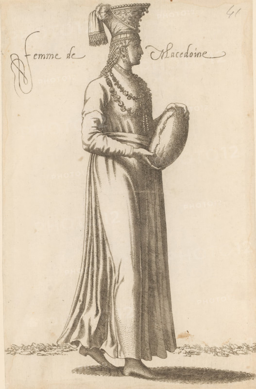 Woman from Macedonia, Femme de Macedoine, print, album page, book illustration, Print is part of an album., printmaker: Léon Davent, after drawing by Luca Penni (attributed to), after drawing by Nicolas de Nicolay (possibly), publisher: Guillaume Rouille (I), Lyon, 1555 - 1568, Attributed to, paper, etching, pasted on album page, height 260 mm x width 169 mm, A tall figure in profile faces right wearing a long, flowing gown with visible folds and a fitted waist, the sleeves extending to the wrists; the figure holds a rounded object in both hands at waist level and wears multiple layered necklaces and decorative chains around the neck and chest; the head is adorned with a tall, pointed headdress featuring a draped cloth and fringe, and long braided hair hangs down the side; bare feet are visible beneath the hem standing on a textured ground, and the image is rendered in fine linework on a light-toned background.