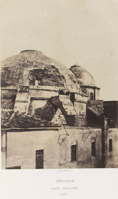 Jerusalem. Saint Sepulcre. Coupole, Dome of the Church of the Holy Sepulcher in Jerusalem, photograph, page, photographer: Auguste Salzmann, Jerusalem, printer (person): Louis-Désiré Blanquart-Evrard, Lille, publisher: Gide et J. Baudry, Paris, 1854 - 1856, printer (person), pasteboard, paper, salted paper print, height 216 mm x width 150 mm, Photo on unnumbered page., parts of church exterior and annexes (with NAME), Church of the Holy Sepulcher, A sepia-toned photograph showing the upper portion of an aged stone building with a large rounded dome in the foreground and a smaller rounded dome behind it, both showing worn and patched surfaces with visible masonry lines; beneath the domes the structure includes heavy buttresses, an arched opening, and a terrace with a metal railing casting shadows onto the wall below; in front of the terrace a lower building with a tiled roof and plastered walls is visible, with several rectangular windows and metal brackets projecting from the wall; the...