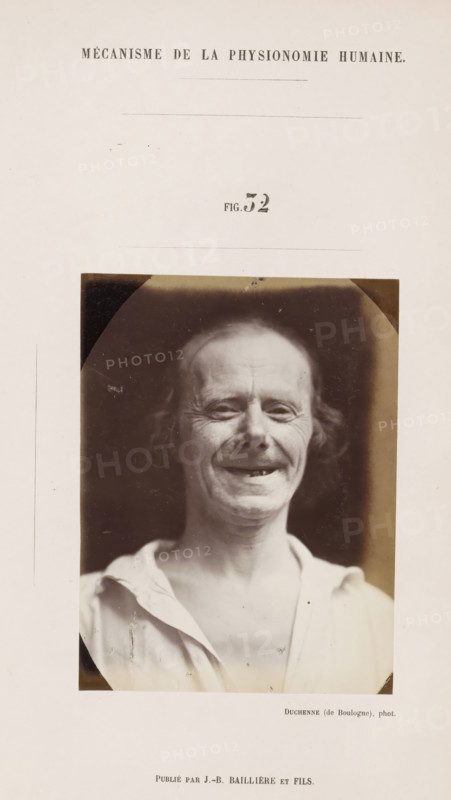 Portrait of a subject: 'un vieillard', photograph, page, Unnumbered page with photo 32 from Mécanisme de la physionomie humaine ou analyze électro-physiologique de l'expression des passions (Atlas)., photographer: Guillaume Benjamin Amand Duchenne, France, publisher: JB Baillière et Fils, Paris, c. 1860 - in or before 1862, Guillaume Benjamin Amand Duchenne, JB Baillière et Fils, photographer, publisher, paper, albumen print, albumendruk, height 120 mm x width 90 mm, experiment, test, science and technology, old man, face, morphology of facial expression, physiology and anatomy, physiognomy, nervous system, neurology, A sepia-toned portrait photograph of an older person with thin hair and visible facial wrinkles, shown from the chest upward against a dark background, wearing a light-colored open-collared shirt and smiling with teeth visible, mounted on a pale page with blank space surrounding the image.