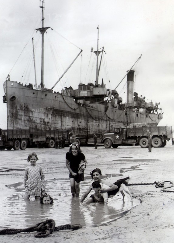 Fillettes jouant sur une plage d'Arromanches, devant un bateau allié