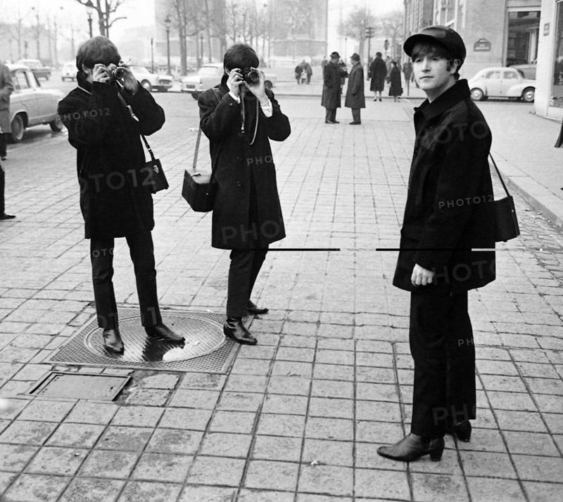 The Beatles on the Champs Elysees before Ringo arrived in Paris later in the  day, Wednesday 15th January 1964.

George Harrison (left) and Paul McCartney taking pictures as John Lennon looks on.