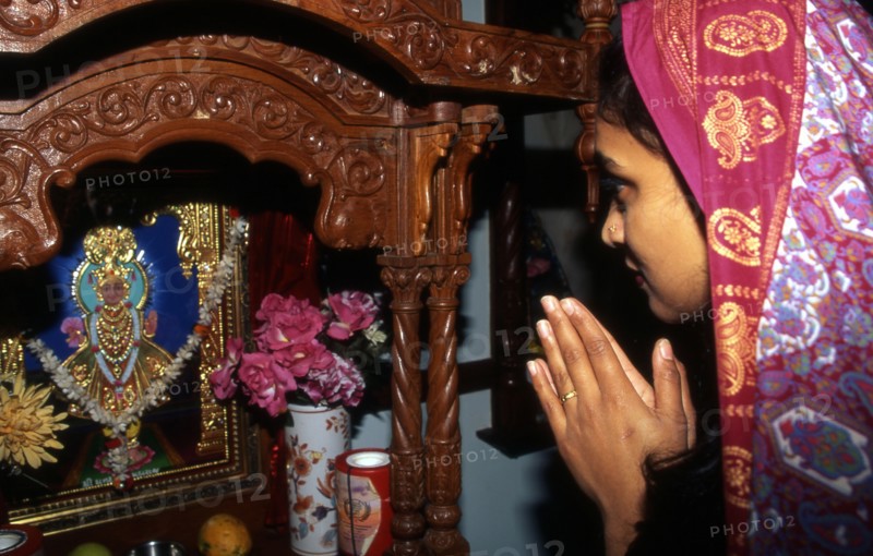 Woman praying before a small 'mandir' in a Hindu temple in the UK