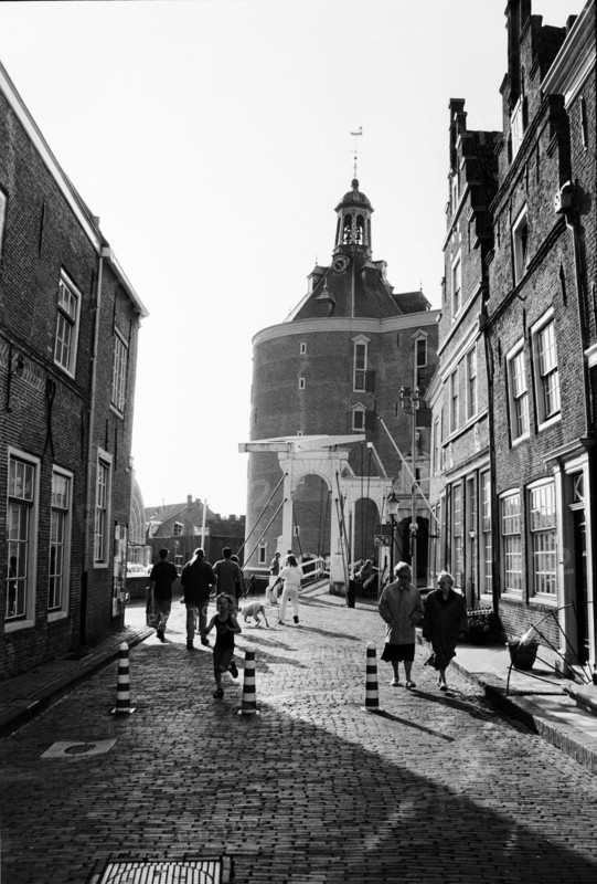 Rue pavée bordée de maisons de briques, avec une tour au fond et des piétons en contre-jour. Enkhuizen, Pays-Bas.
1999
