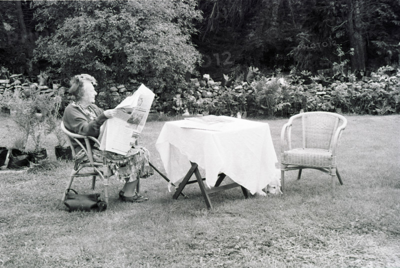 Person reading in a garden, next to a table covered with a white tablecloth.
2000