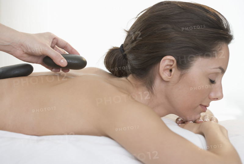 Masseuse placing stone on woman's back.