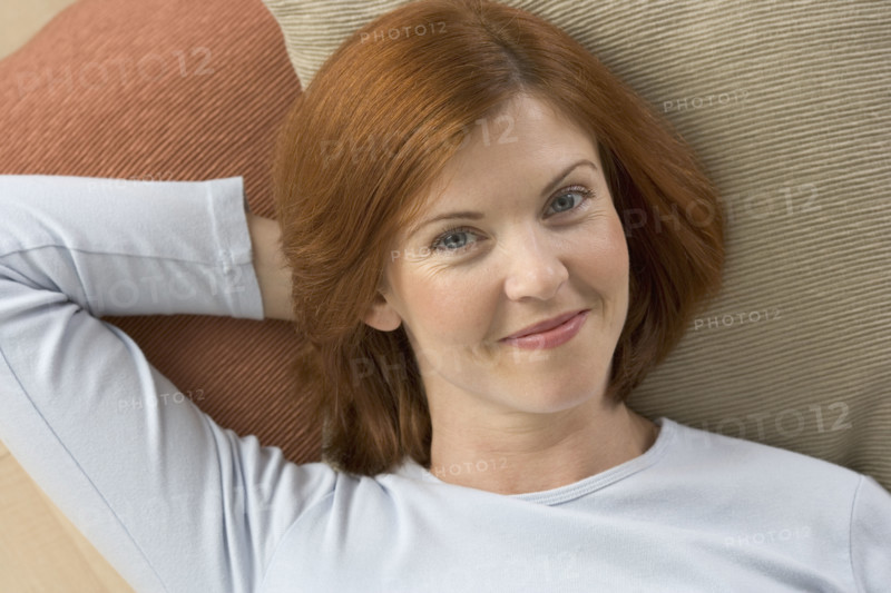 Smiling redheaded woman lying on pillows.