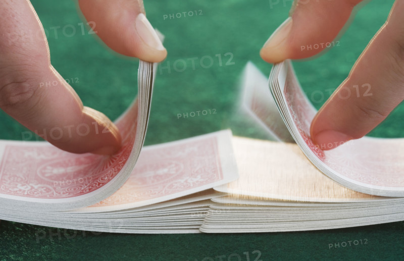 Hands shuffling cards on poker table.