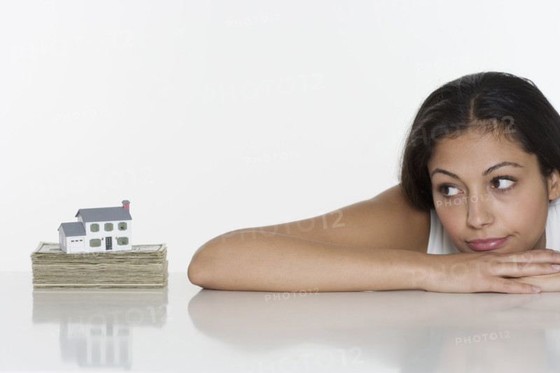 Woman looking at miniature house and money.