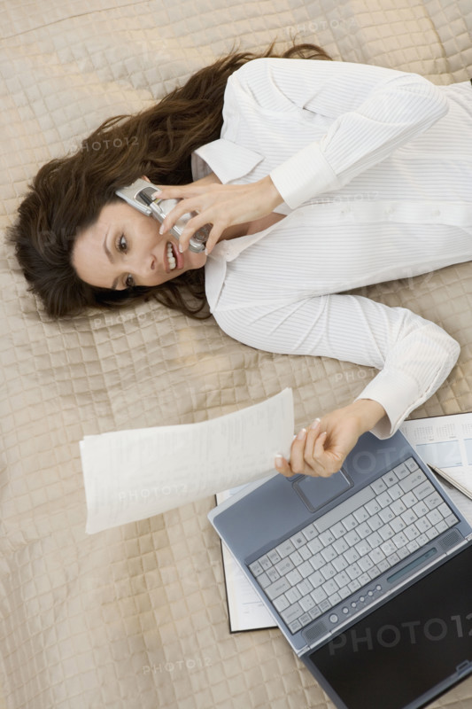 Businesswoman on mobile phone while lying on bed.