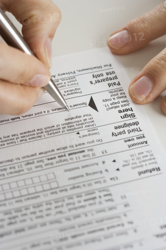 Closeup of hands signing tax form.
