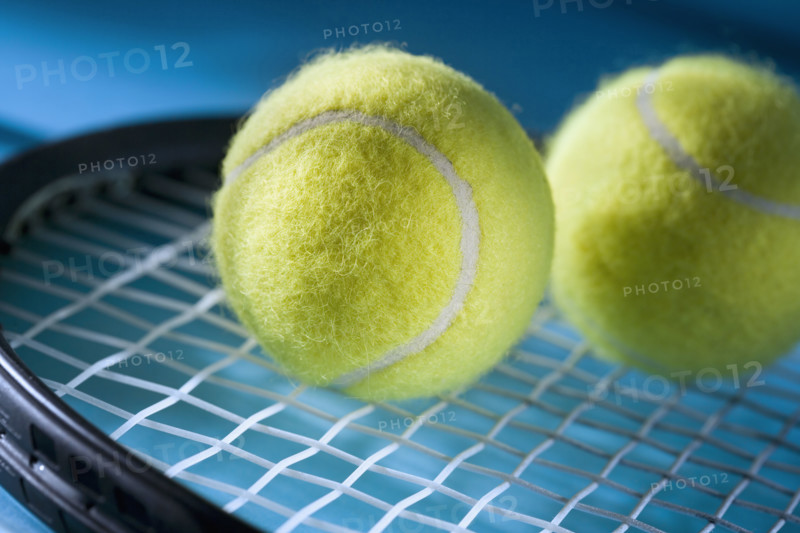 Closeup of tennis racquet and two balls.