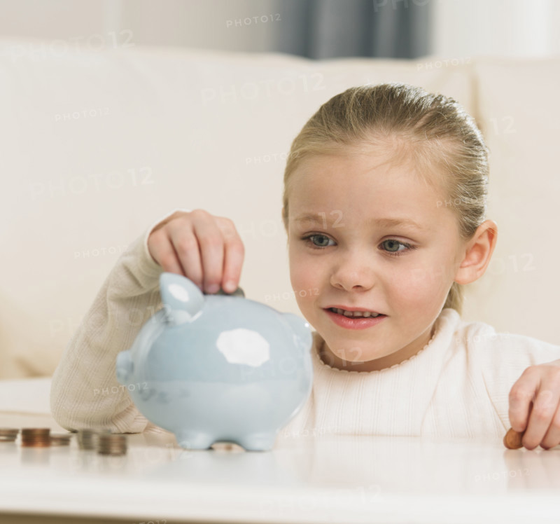 Young girl putting change in piggy bank.