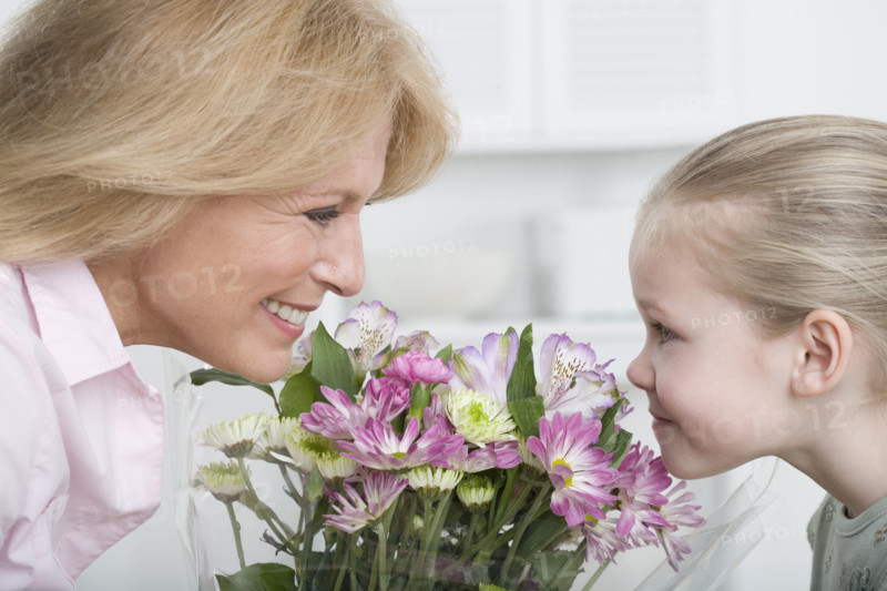 Grandmother and young granddaughter smelling bouquet of flowers.