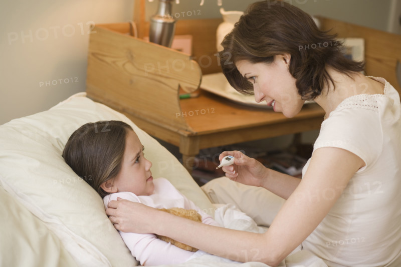 Mother checking young daughter’s temperature with thermometer.