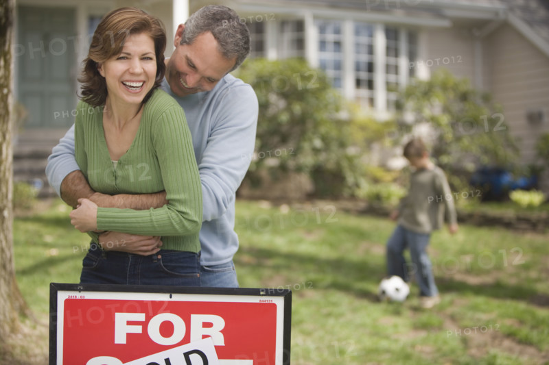 Family in front of house with For Sale/Sold sign.