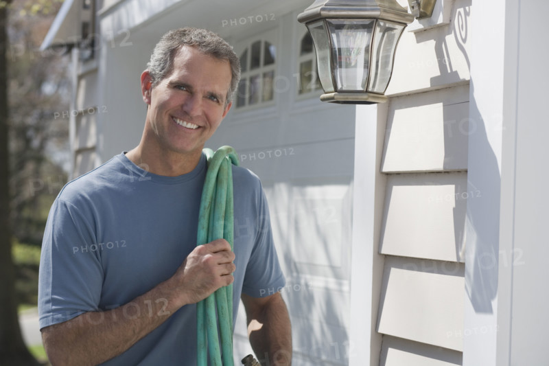 Man holding hose in front of garage.