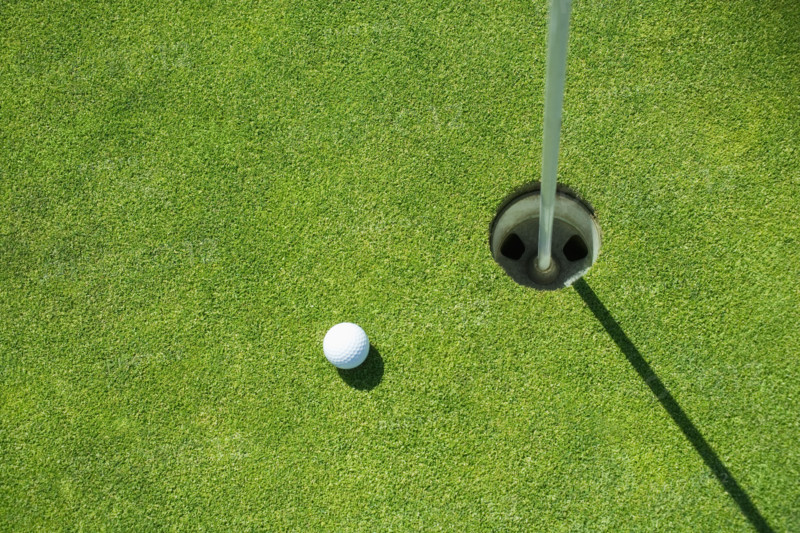 Golf ball near cup on putting green outdoors.