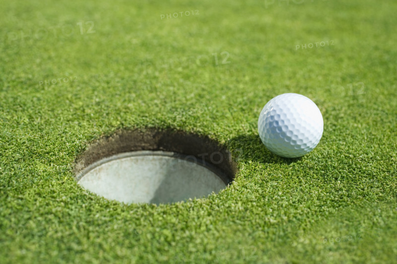Golf ball near cup on putting green outdoors.
