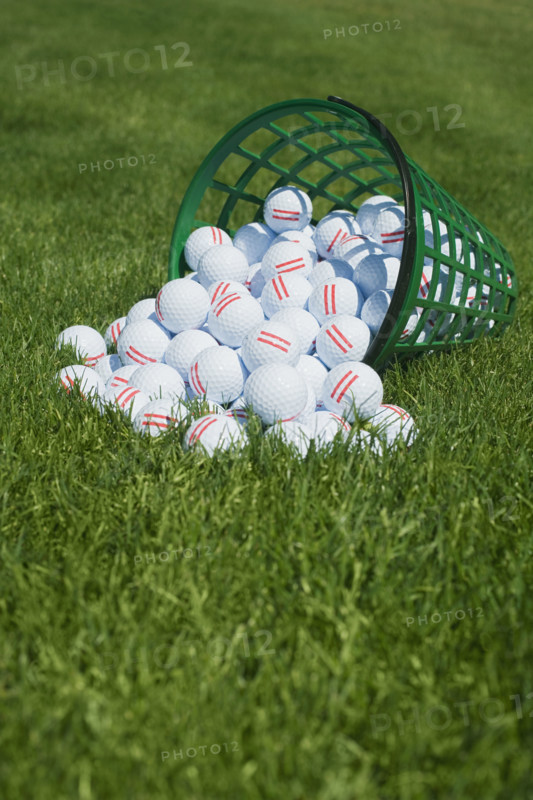 Basket of golf balls spilling onto grass.