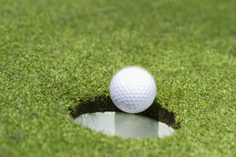 Golf ball dropping into hole on green.