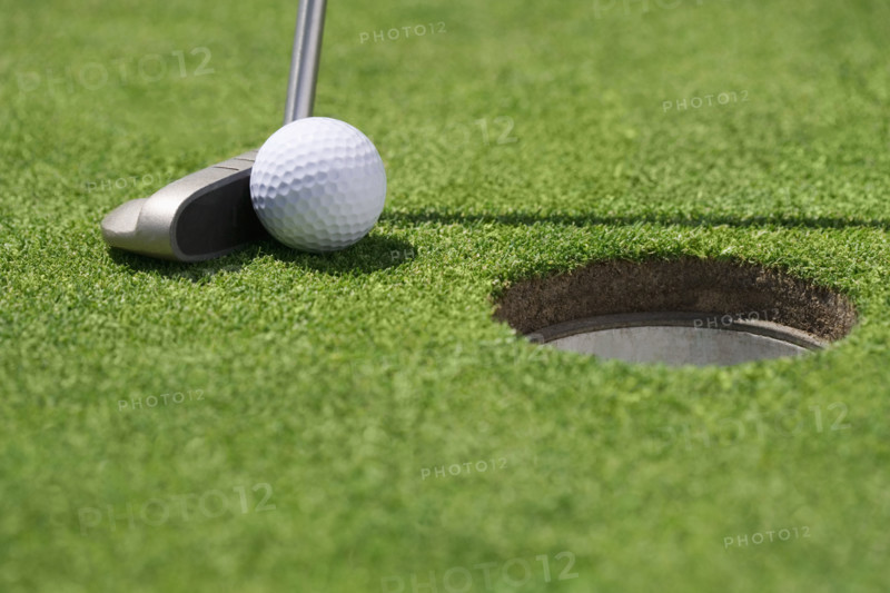 Closeup of golf ball and club near cup.