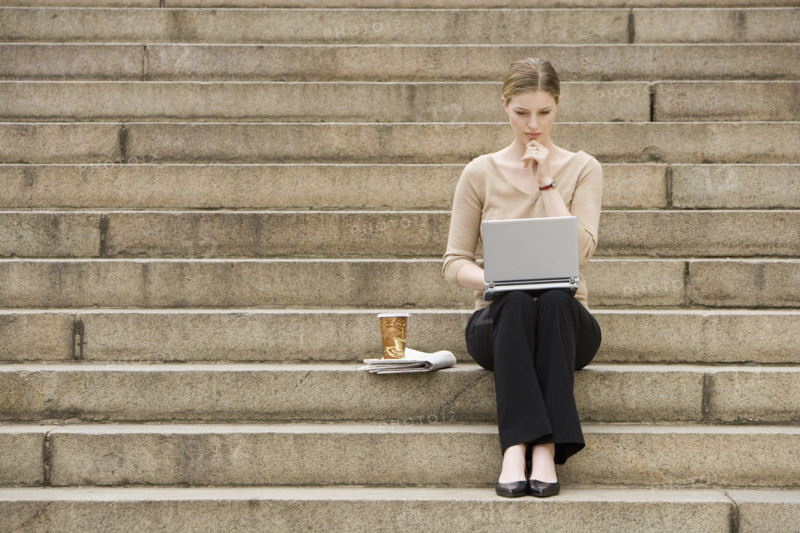 Young woman sitting outdoors on stairs with laptop.