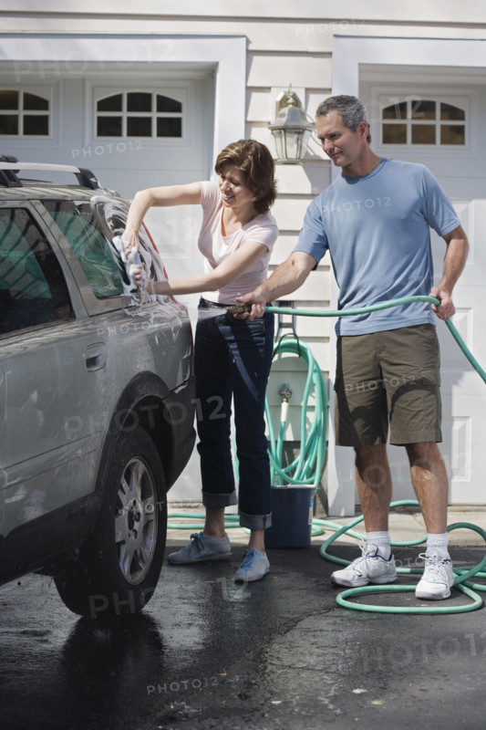 Couple washing car in driveway.