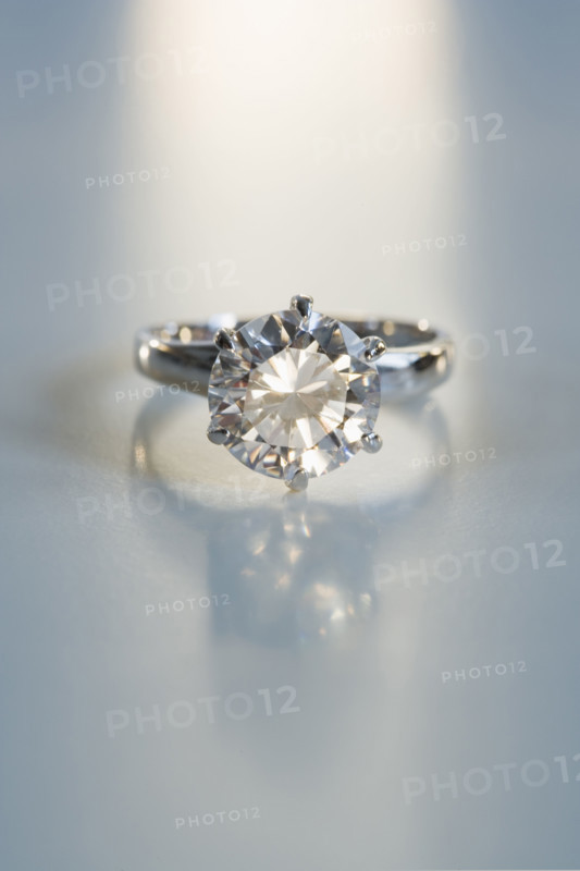 Diamond like ring in six pronged silver setting on table.