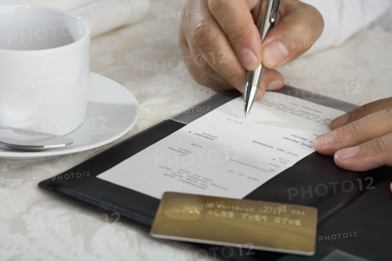 Close up of man signing credit card receipt at restaurant.