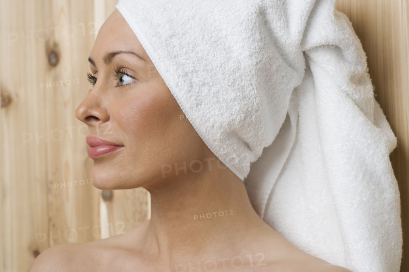 Woman in sauna with head wrapped in towel.