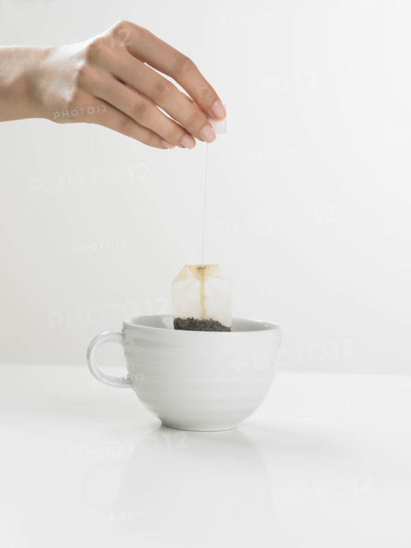 Studio shot of tea cup with woman's hand holding tea bag.