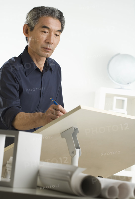 Asian businessman at drafting table with blueprints.