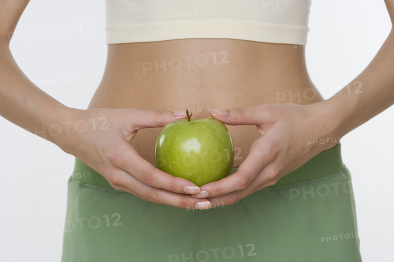 Studio shot of woman holding apple in front of belly.