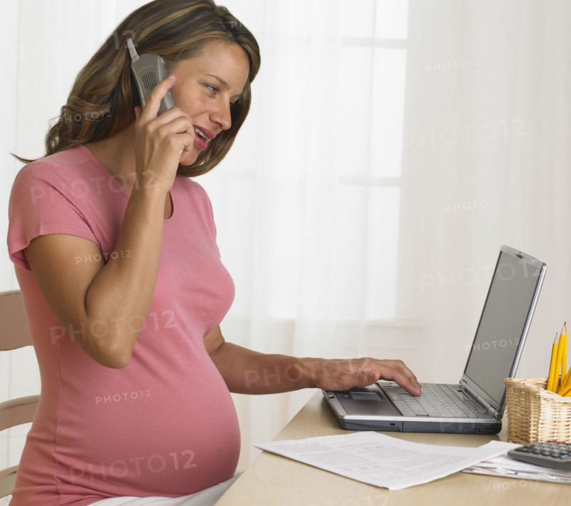 Pregnant woman using telephone and laptop.