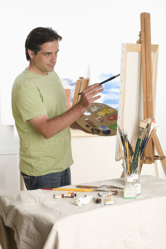 Man painting at easel indoors.