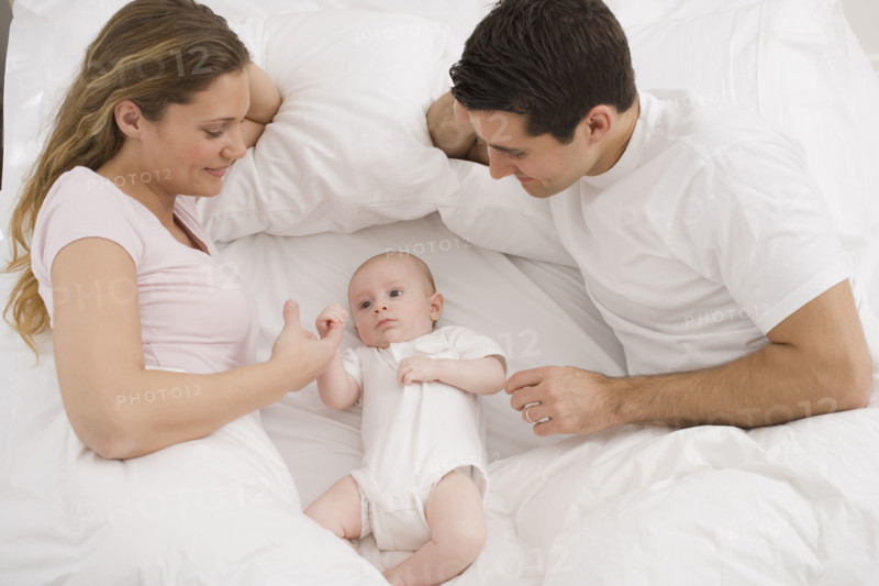 Parents smiling at baby in bed.