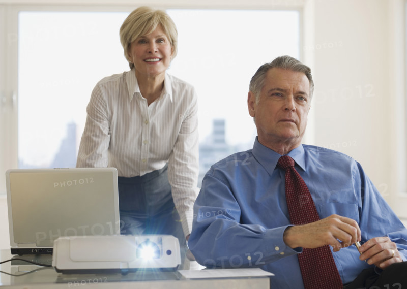 Senior businesspeople using projector in conference room.