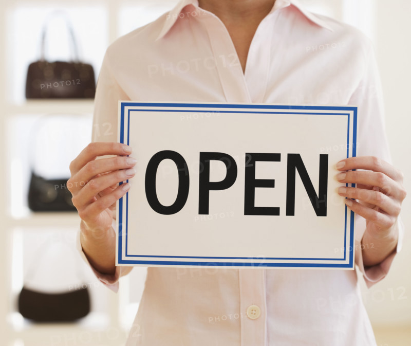 Woman holding Open sign in boutique.